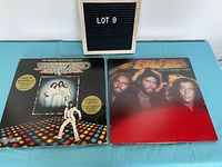Two Bee Gees vinyl albums side by side, Saturday Night Fever featuring John Travolta dancing, and Spirits Having Flown with three Bee Gees members on cover.