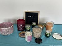 Photo showing assorted candles and a pink candle holder on a blue surface against a white wall. Includes multiple candles in glass jars and small tealights.