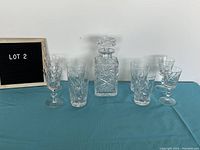 Wide view of the crystal decanter, whisky tumblers, and aperitif glasses arranged on a blue cloth.