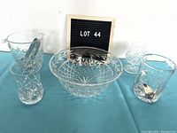 Five Edinburgh crystal items on blue cloth: large ice bucket with metal tong, large bowl, pitcher, stemmed brandy snifter, small vase