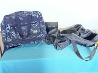 Two duffle bags displayed side by side, with the floral rolling bag on the left and black nylon duffle on the right.