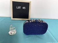 Royal blue rhinestone encrusted evening clutch bag with silver bow clasp and metal chain strap, placed on blue surface with a black felt letter board showing 'LOT 45' in background