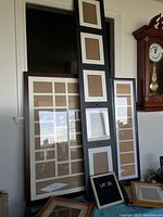 Photo showing assorted large and medium multi-picture collage frames leaning against a wall next to a clock.