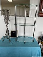 Glass and metal corner shelf with three curved glass shelves and metal support rods in a triangular corner shape.