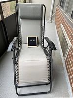 Full front view of light gray fabric gravity chair showcasing padded headrest and black metal frame on a balcony.