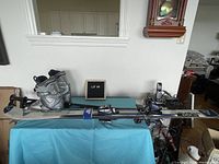 Full display of the skis, ski boots, and poles arranged on a blue surface in an indoor setting.