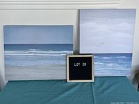 Two canvas prints of ocean seascapes, one landscape and one portrait. Both 16x20 inches, placed side by side with a sign indicating Lot 26.
