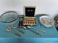 Photo of assorted stainless steel and silverplate serving pieces along with ceramic pie plate and glass bowl on blue tablecloth