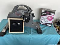 Sunny Health & Fitness stationary pedal exerciser with Forever Flex stability ball box and Lot 39 sign on a blue cloth-covered table.