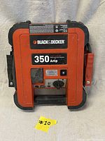 Front view of the Black & Decker 350 Amp Jump Starter showing the orange and black casing with labels, power switch, lamp, and attached jumper cables.