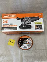 Boxed Warrior angle grinder and 10 pack of cutoff wheels on a grey fabric surface