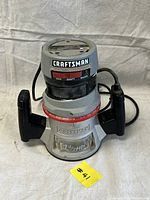 Front and side view of Craftsman router showing handles, motor housing, and branding with power cord.