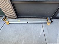 Full view of the DeWALT miter saw stand lying on concrete outdoors, showing the extendable support bars and overall length.