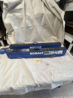 Full view of two folded Kobalt 42-inch folding sawhorses resting on a white cloth, showing blue metal construction with black rubber grip tops and Kobalt branding.