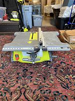 Angle shot of the table saw showing the blade area, adjustment mechanisms, and part of the stand on a carpet.