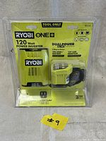 Front view of Ryobi One 120 Watt Power Inverter in original package showing product name, wattage, connection options, and 120V outlet.