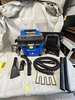 Front view of the Vacmaster vacuum with accessories laid out including hose, nozzles and extension tubes.