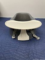 Front view of gray Bumbo baby chair with attached white food tray and visible safety straps.