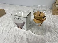 Chemex glass coffeemaker with wooden collar and box of Chemex filters on table.