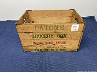 Front side of wooden box showing Eaton's green grocery box branding and instructions for folding and returning the box.