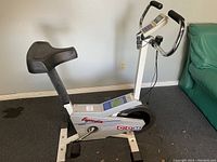 Side view of the CCM Ergometer 3000 exercise bike showing white frame, black padded adjustable seat, and pedal crank area with branding.