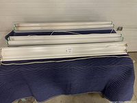 Three 48-inch white metal fluorescent light fixtures placed on a blue padded surface, showing green-tipped tubes and cords