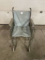 Front view of hospital wheelchair showing gray fabric seat and backrest, padded armrests, and front caster wheels.
