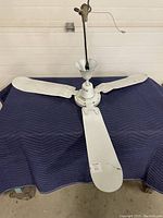 Full view of three-blade white industrial ceiling fan laid flat, showing the fan's overall condition and size.