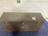 Closed toolbox front view showing two locking latches, lock with keyhole, and overall dark brown finish with light wear.