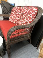 Side angle view of outdoor love seat showing dark brown wicker frame and red cushions with white geometric pattern on back cushions.