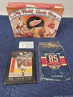 Photo showing the front of Gordie Howe Frosted Flakes cereal box featuring Detroit Red Wings players, the framed plaque of Wayne Gretzky, and an unopened New York Rangers pennant with 85th anniversary logo.