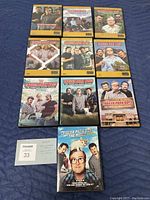 Front sides of all eleven DVD cases laid out on a blue fabric surface, showing the cover art and titles for Trailer Park Boys seasons 1-10 and the movie.
