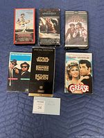 Front view of six VHS tapes on a blue surface: Crossroads, Apollo 13, The Sting, Blues Brothers, Star Wars Special Edition, Grease 20th Anniversary Edition.