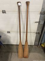 Pair of wooden canoe paddles leaning against a garage door, showing full length and blade shape.