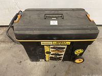 Front view of black and yellow Workforce mobile tool chest with wheels and retractable handle. Shows label and wheels.