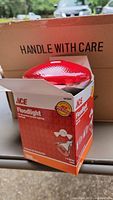 Open box showing red glass floodlight bulb inside an Ace branded box with product information visible.