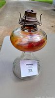 Full view of the antique style oil lamp showing the heavy glass base, colored glass reservoir, and metal burner top.