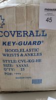 Cardboard box with blue text describing disposable coveralls, 25 pieces size XXXXL, hood, elastic wrists and ankles, style CVL-KG-HE, made in China.
