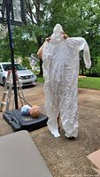 Photo of a white disposable coverall held up by a person outside, showing overall design with hood, elastic wrists and ankles.