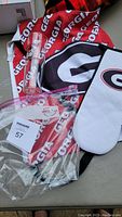 Photo of Georgia Bulldog apron, white oven mitt with Bulldog logo, and vintage tall clear beer glass with Montana Brewing Company logo.
