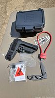 Photo showing EOTech EcoTech storage box, black AR rifle stock, sealed plastic bag, red lock and Gerber folding knife partially open.
