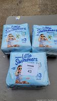 Three packs of Huggies Little Swimmers Size 3 disposable swim diapers arranged on a table.