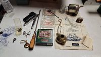 Full lot overview on flat surface showing various vintage collectibles including coasters, ashtrays, tools, and fabric cloth with ship print