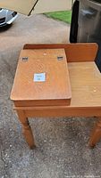 Photo of vintage wooden student desk showing the hinged writing surface with latch and light wood grain finish.