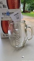 Clear glass football-shaped mug with detailed stitching and textured surface, placed in front of its original Room 2 Room box and a sales tag.