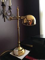 Overall side view of the adjustable gold tone metal desk lamp standing on a surface, showing the arm and dome shade.