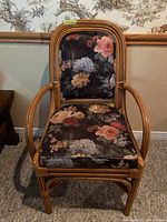 Front view of wood and rattan chair with floral upholstered seat and backrest, showing curved armrests and detailed floral fabric pattern.