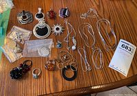Full collection on wood table showing assorted costume jewelry including chains, pendants, rings, brooch, and earrings