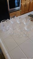 Seven crystal stemware glasses arranged on tiled counter with a small pitcher in the back, showing the entire set.