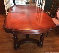 Full view of the wood dining table showing the main surface with detailed wood grain pattern and rounded edges, supported by thick turned legs.